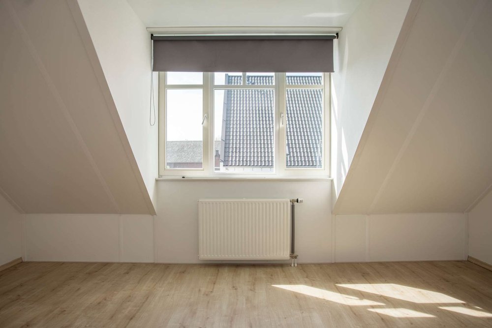 Intérieur sous combles illuminé par une lucarne rampante offrant une vue verticale et une hauteur sous plafond confortable