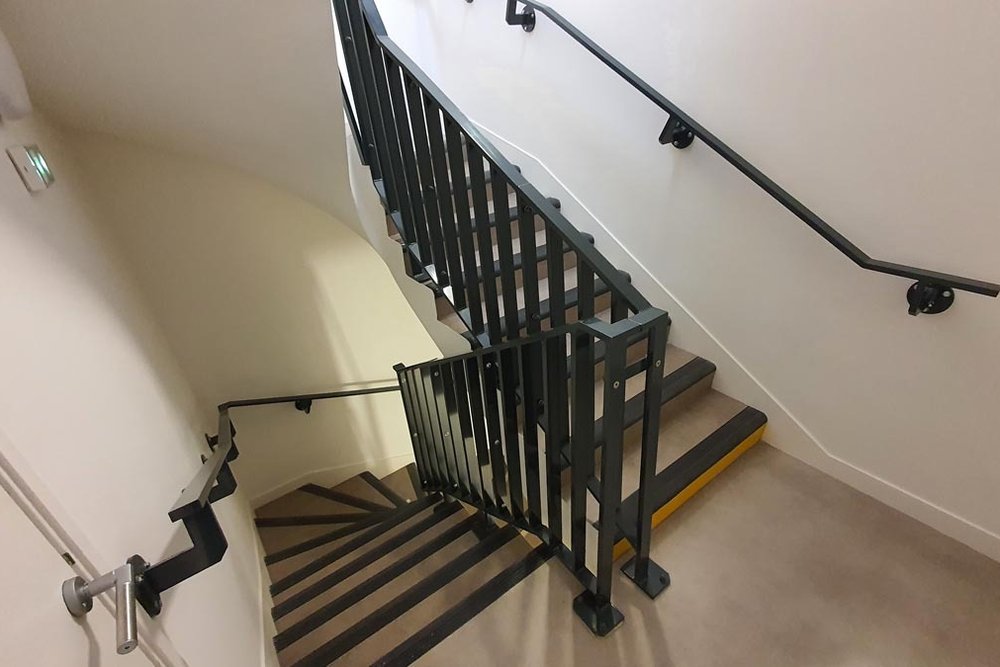 Cage d'escalier d'immeuble conforme aux normes PMR avec nez de marches contrastés et main courante continue