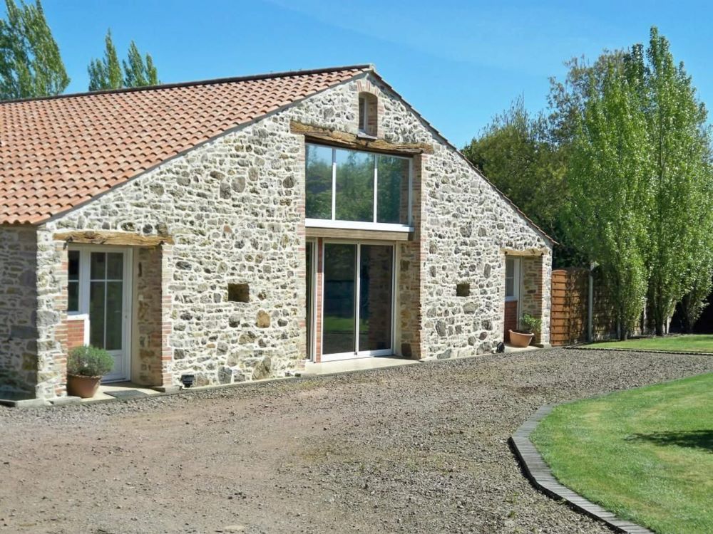 Façade d'une grange en pierre rénovée et convertie en logement avec nouvelles fenêtres en bois