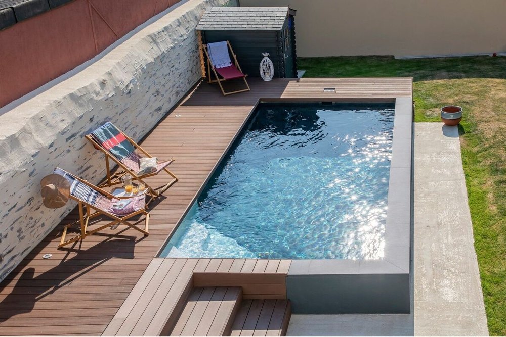 Vue d'une piscine semi-enterrée avec terrasse bois respectant la marge de recul par rapport à la clôture mitoyenne