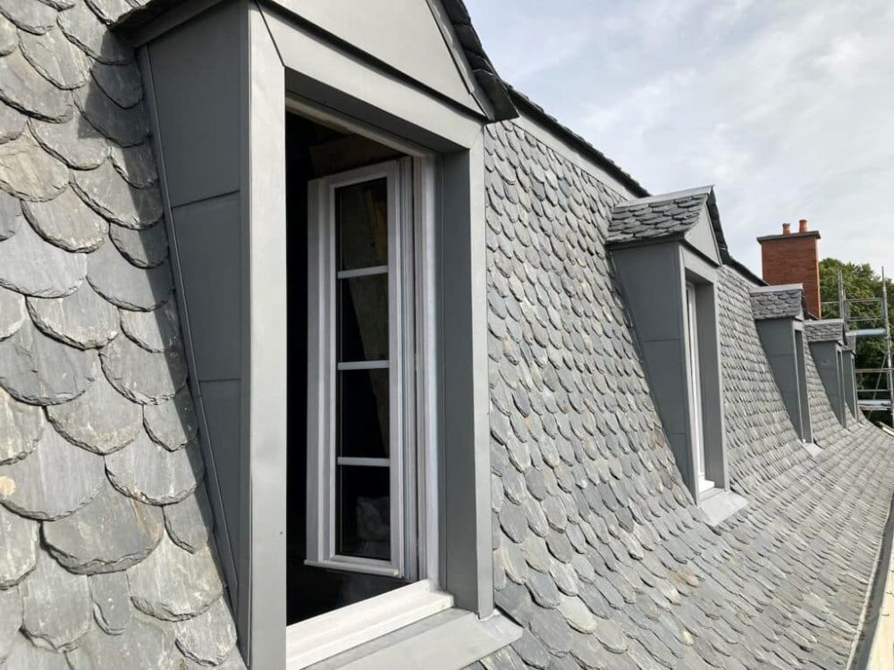 Lucarne avec joues en zinc et couverture en ardoise assortie à la toiture principale du bâtiment