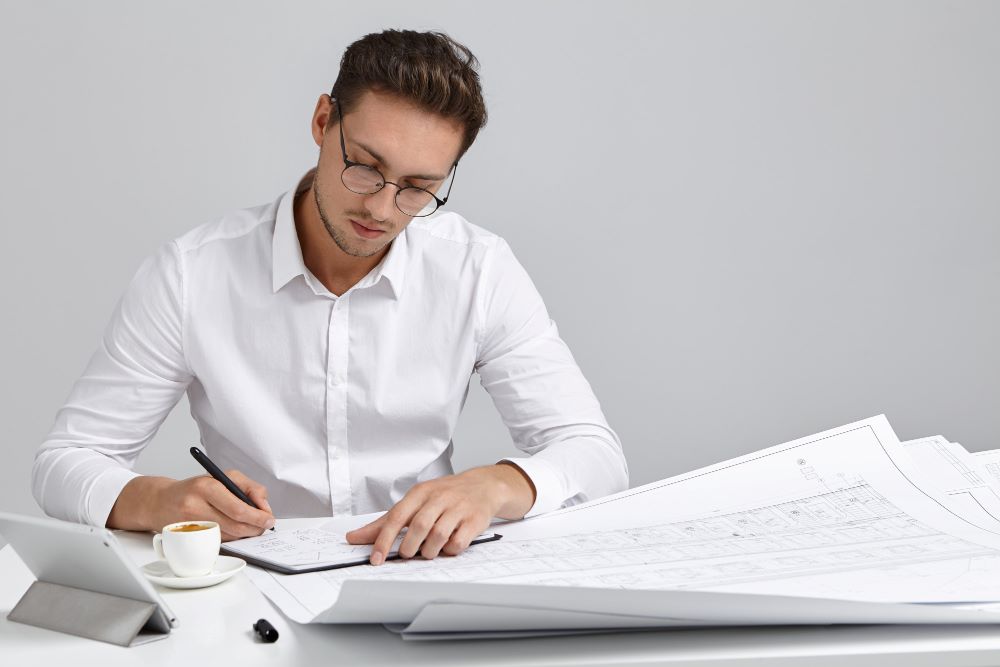 Rédaction de la notice descriptive d'un dossier de permis de construire avec plans et documents sur un bureau