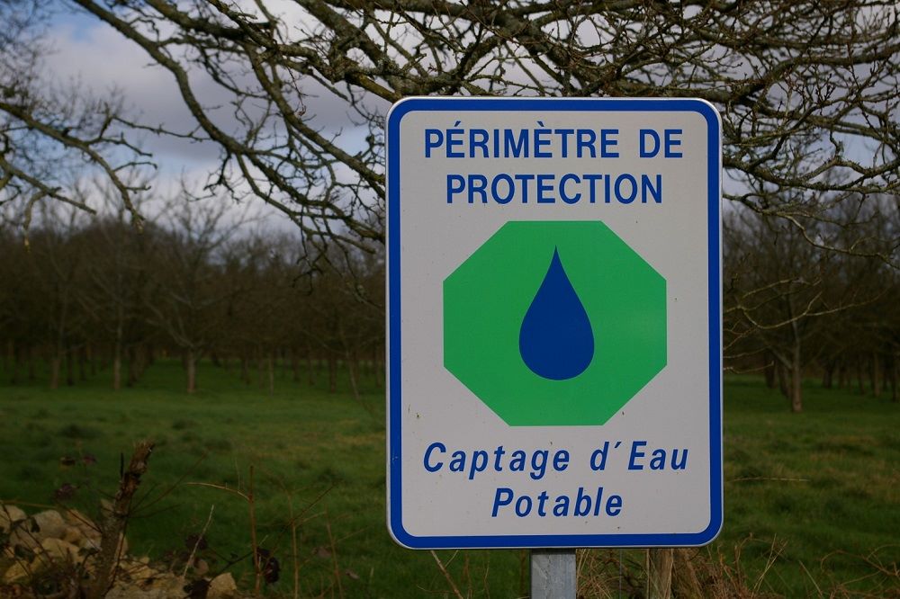 Captage d'eau potable entouré de sa clôture de périmètre de protection immédiate avec panneau d'interdiction