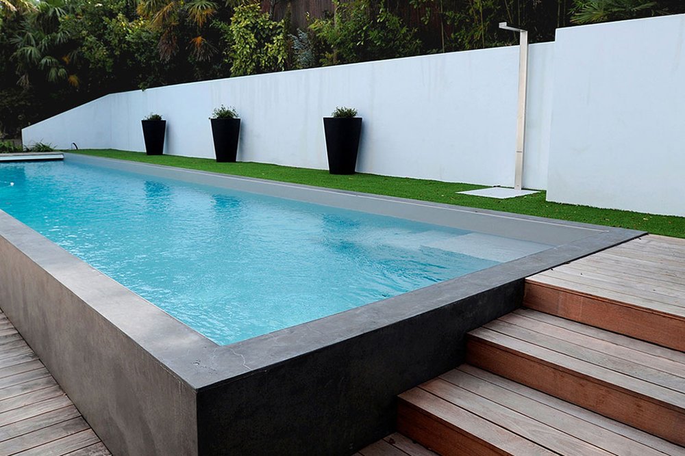 Bassin de piscine semi-enterré implanté en dénivelé sur un terrain en pente avec plage en bois et maçonnerie