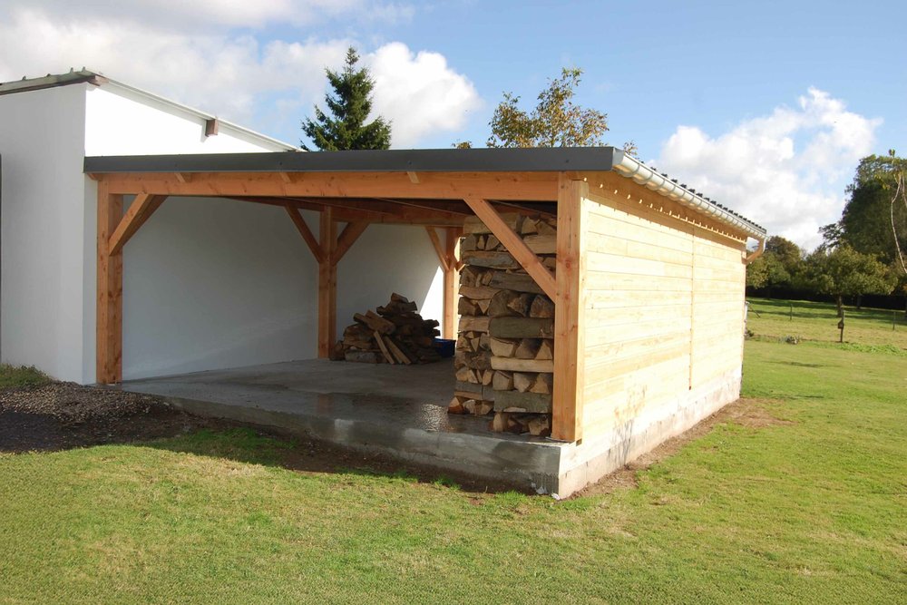 Préau à structure bois avec poteaux et toiture en tuiles abritant une zone de circulation entre la maison et le garage