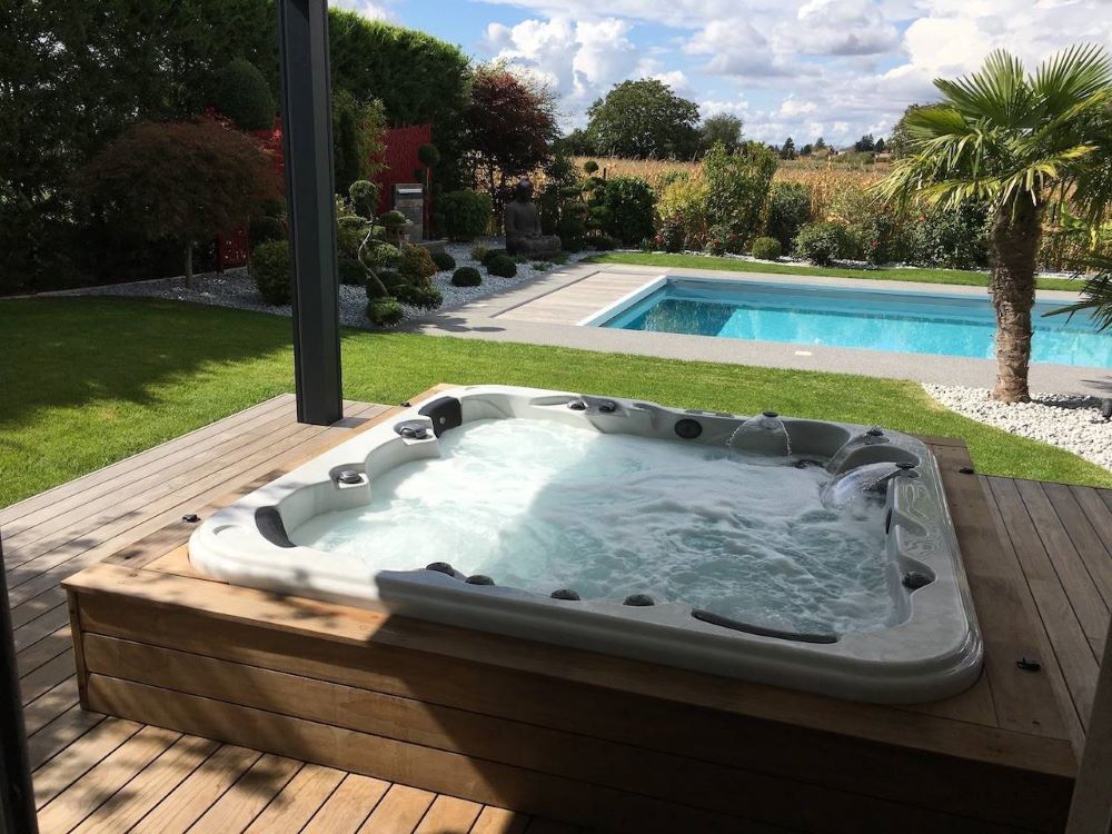 Spa jacuzzi extérieur haut de gamme installé dans le jardin d'une maison individuelle avec terrasse en bois